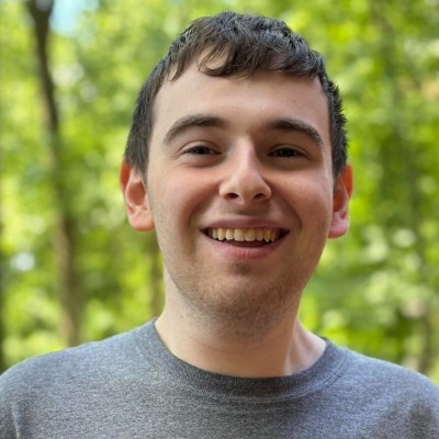 A picture of Max Richman smiling in front of trees